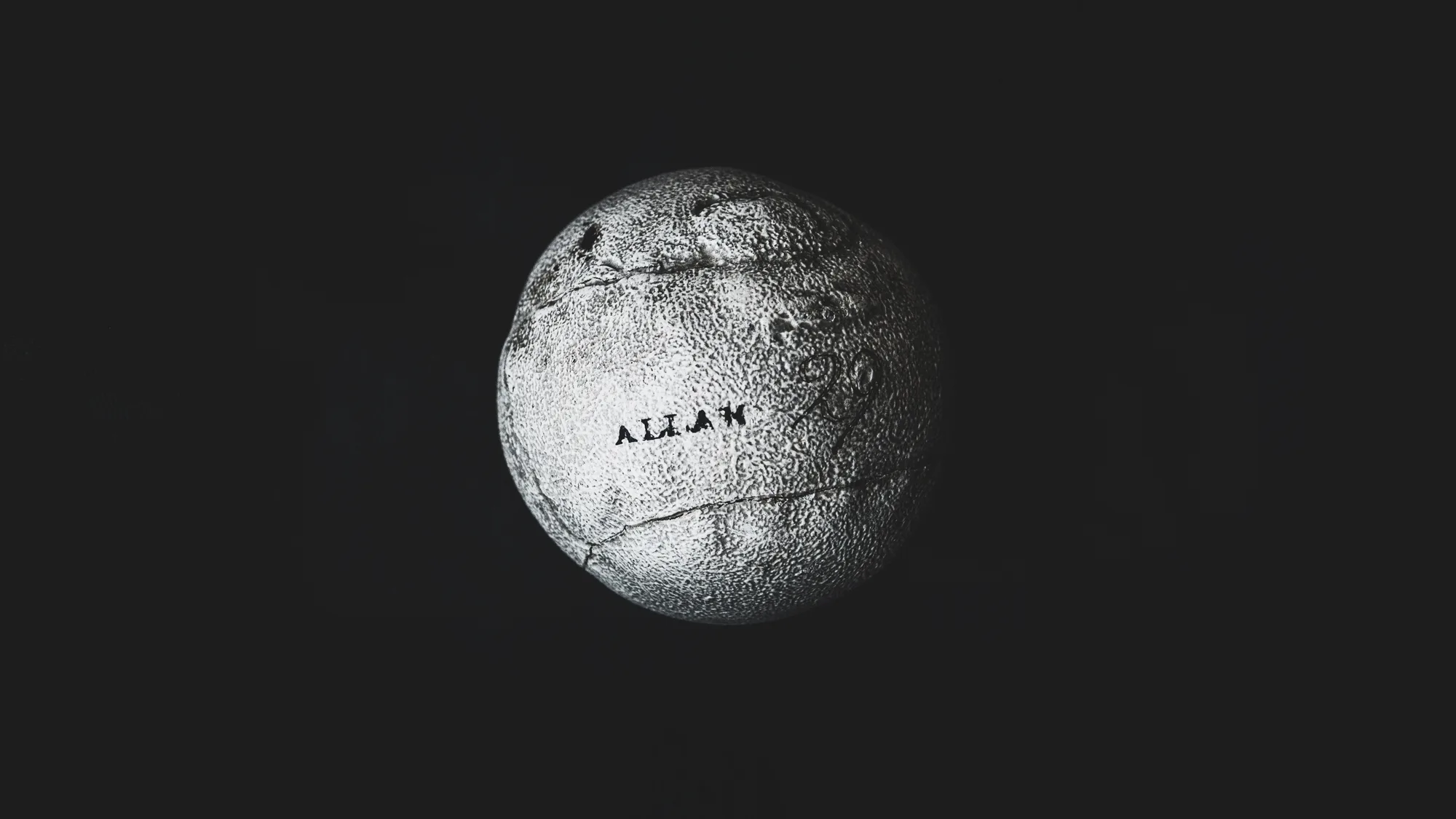 A single worn feathery golf ball stamped ALLAN, lit against a black ground